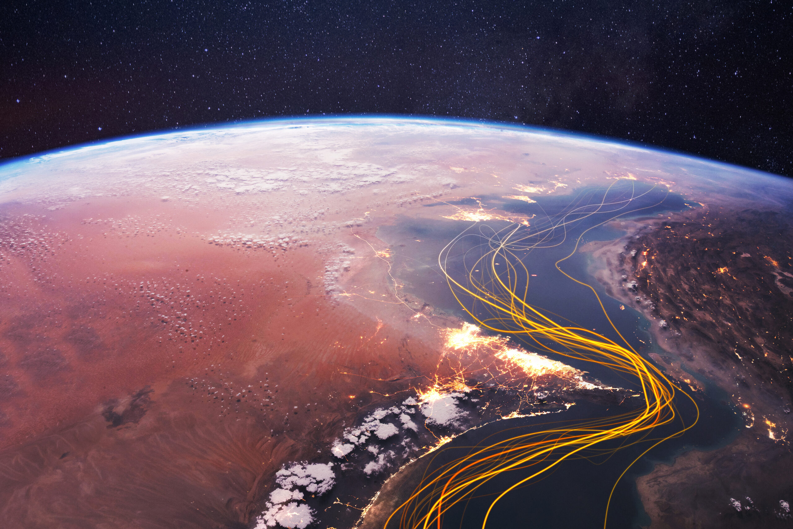 Earth's curved horizon from space over a desert coast, with starry sky above and glowing flight paths across Africa at dusk/night.